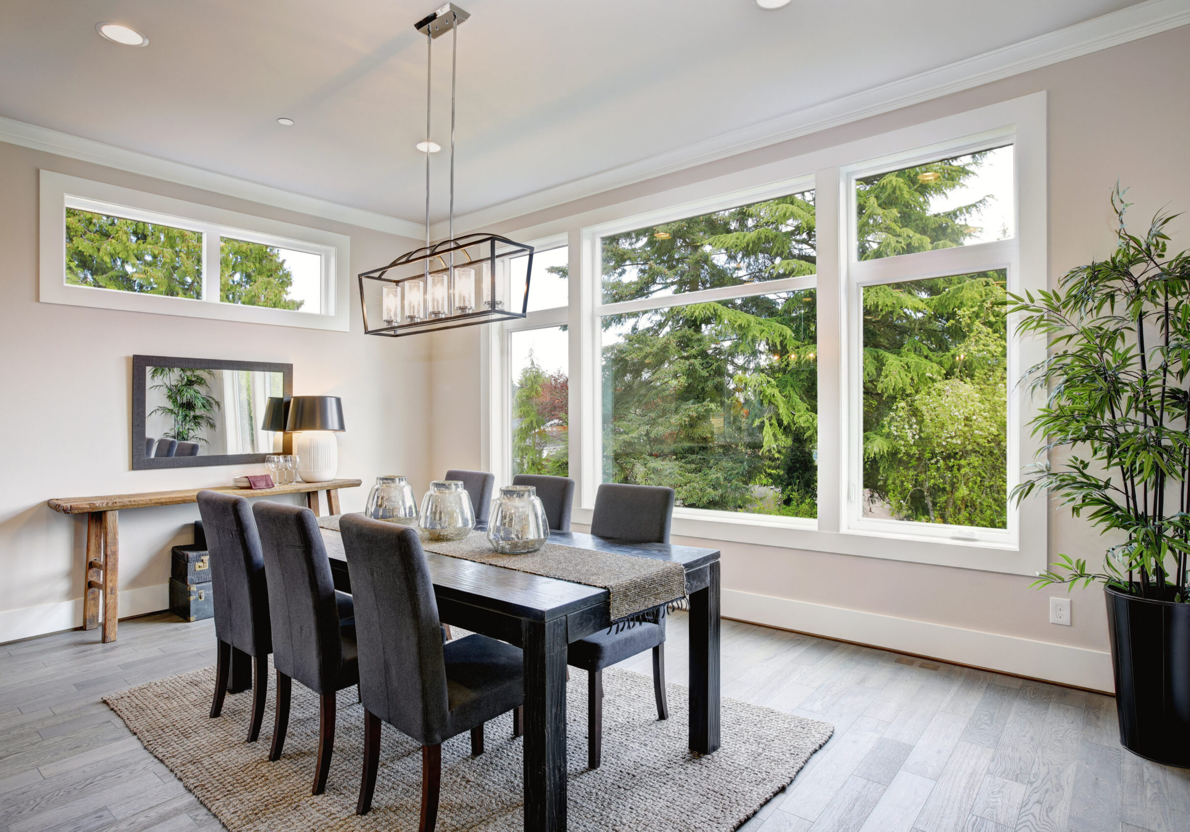Luxurious modern dining room boasts a black dining table illuminated by a rectangular chandelier and surrounded by gray velvet dining chairs over taupe sisal rug finished with rustic console table.