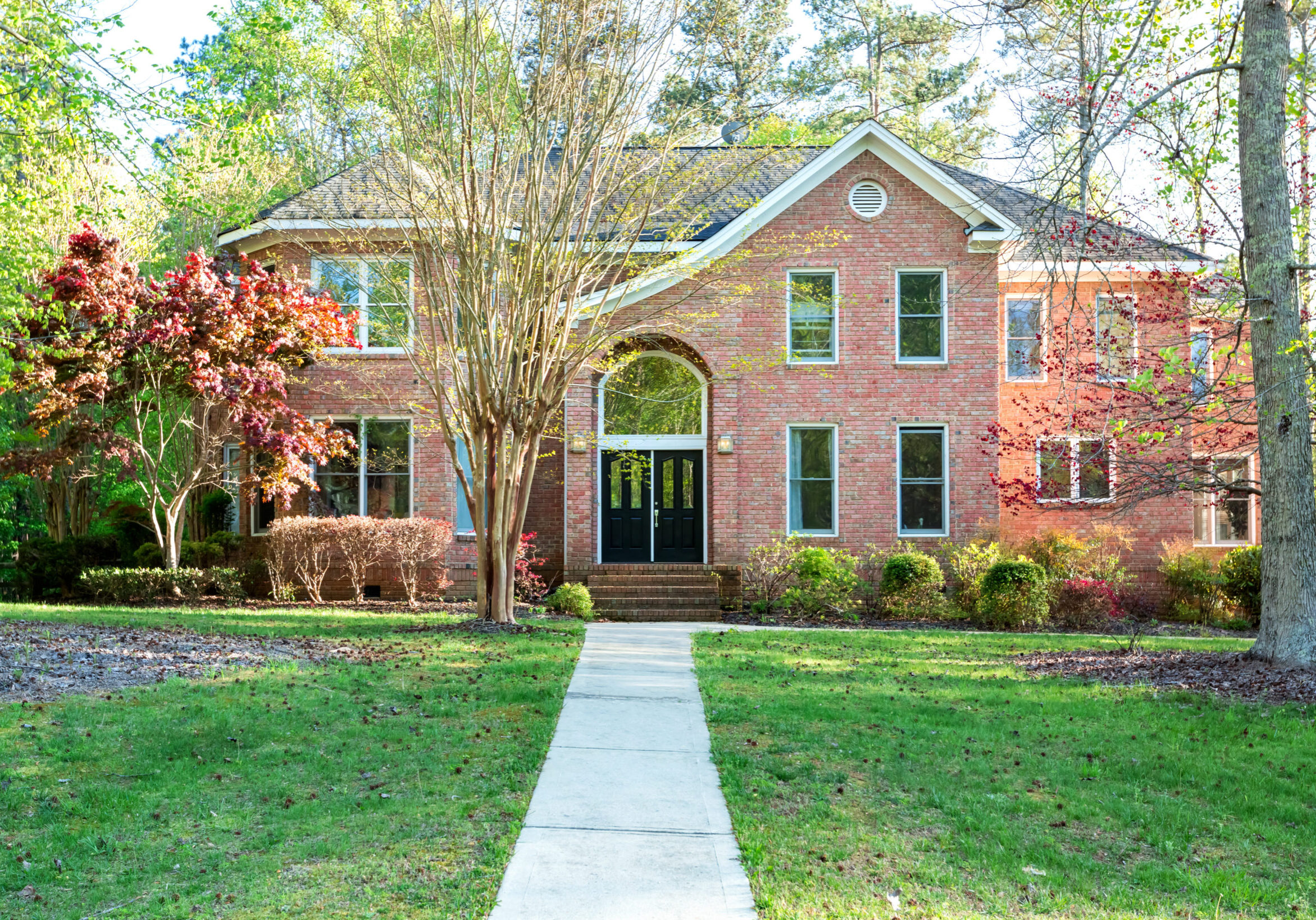 Two-story brick home in Tucker, Georgia, with symmetrical grid windows and a double black front door, surrounded by trees.