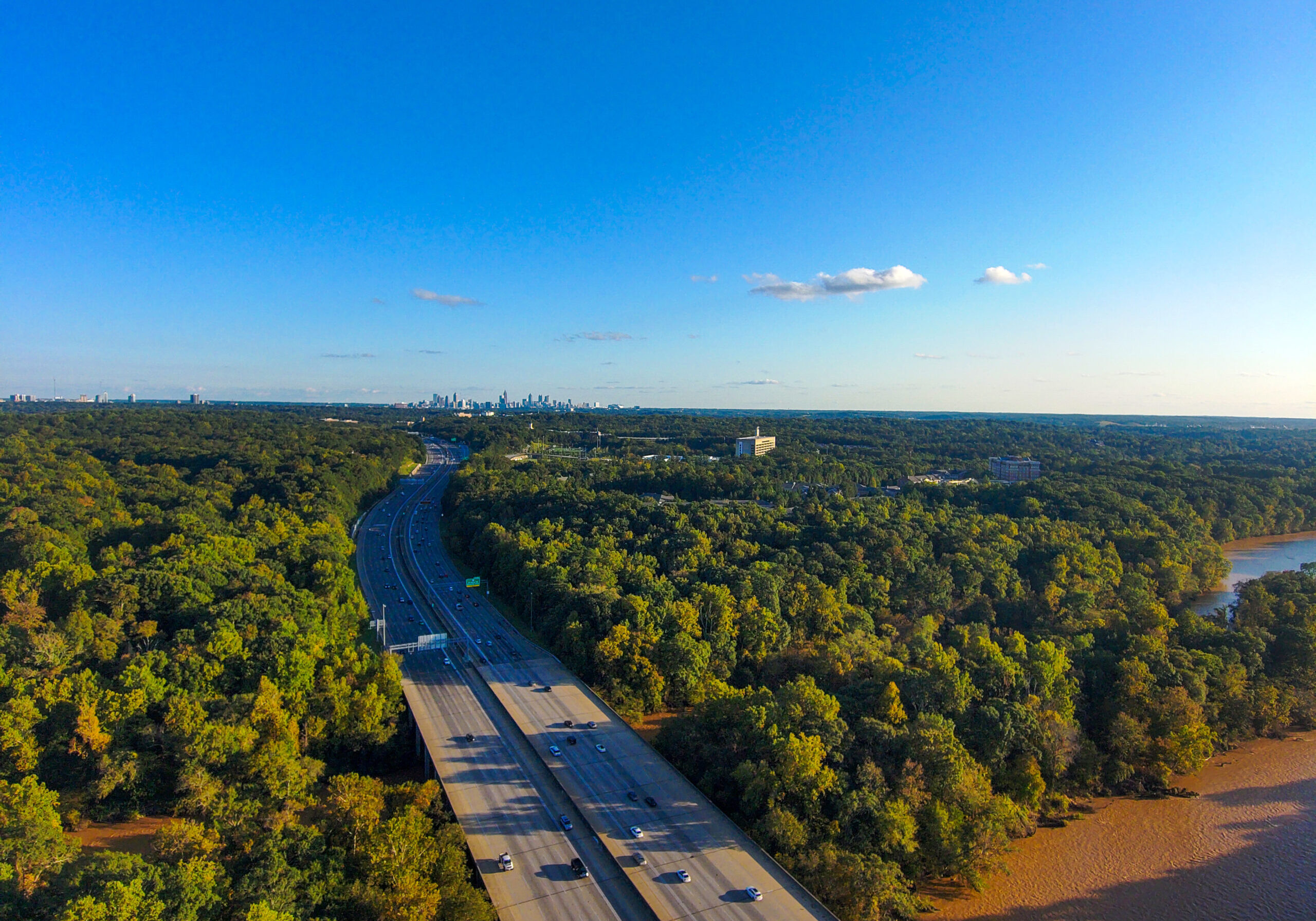 Aerial view of highway passing through dense forest in Atlanta suburb of Sandy Springs, Georgia, with city skyline in distance.