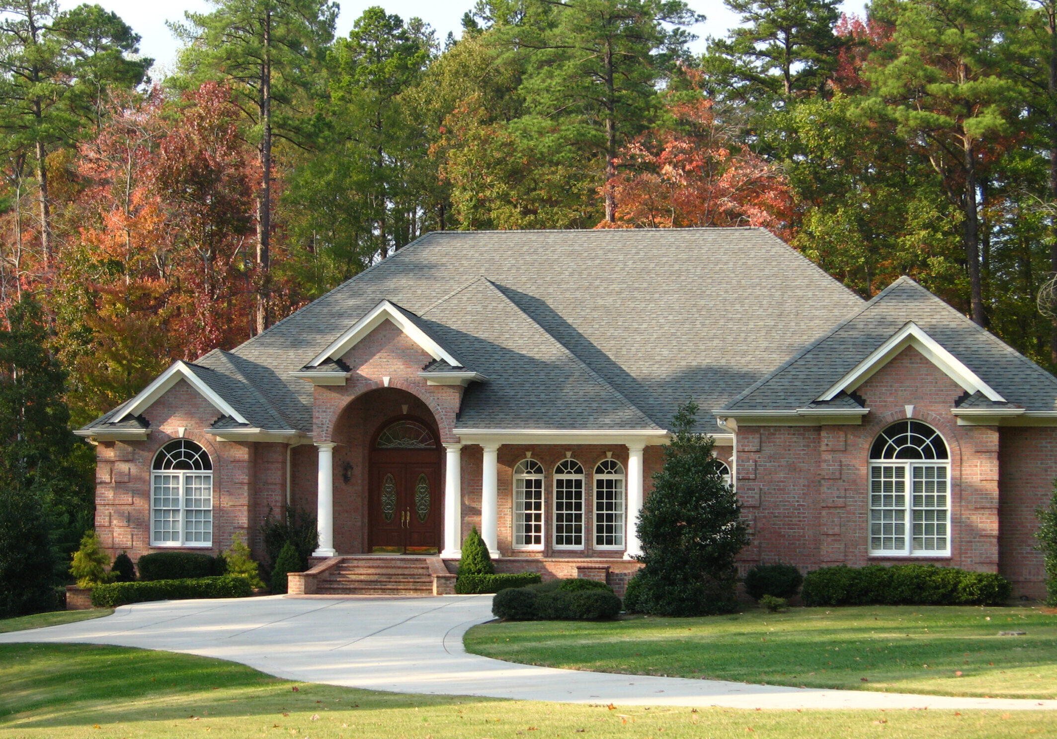 Elegant brick home in Norcross, Georgia, with arched grid windows, double wood front door, columned porch, and manicured lawn.