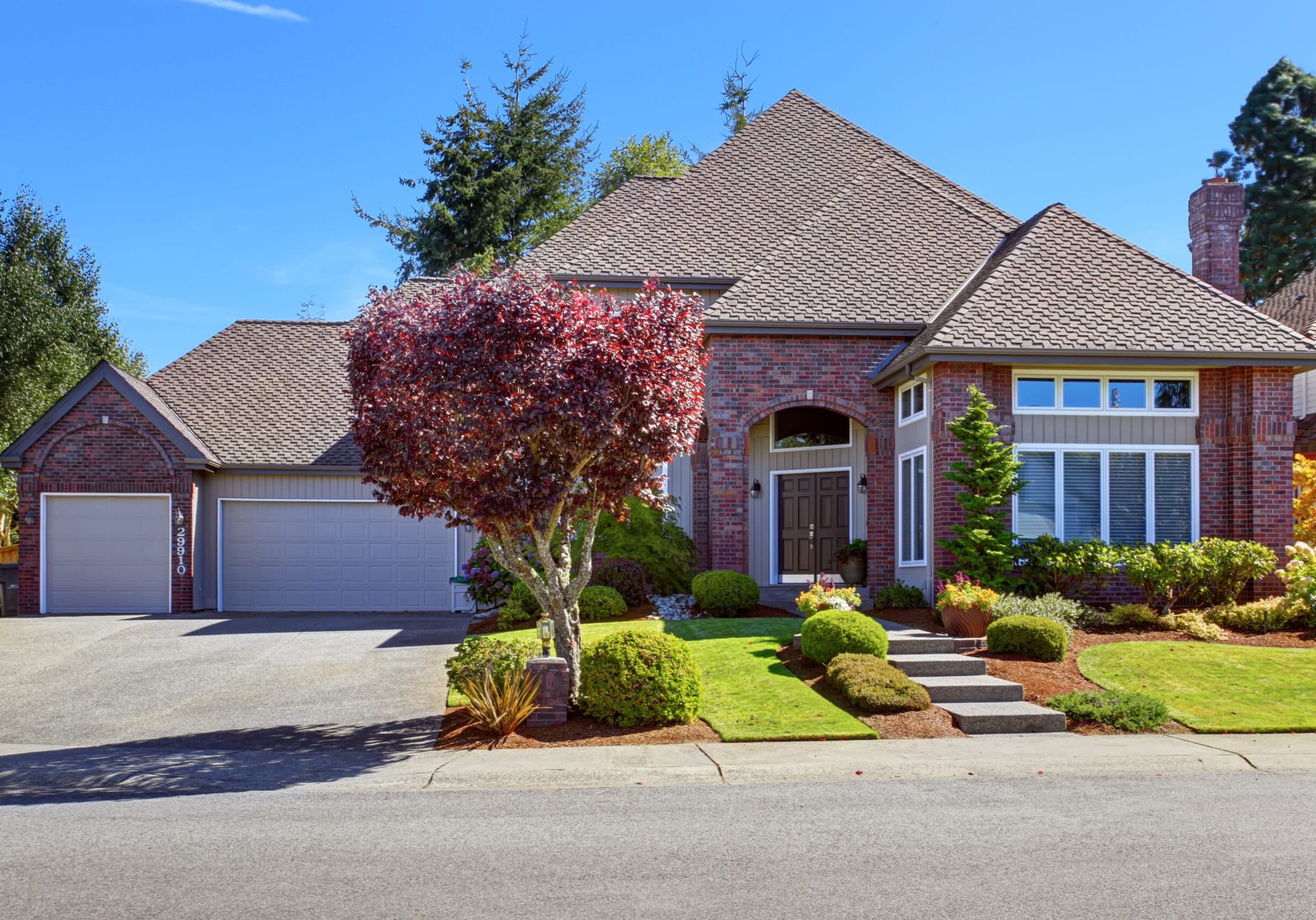 Big luxury house with tile roof and brick wall trim. Walkway decorated with flower pots