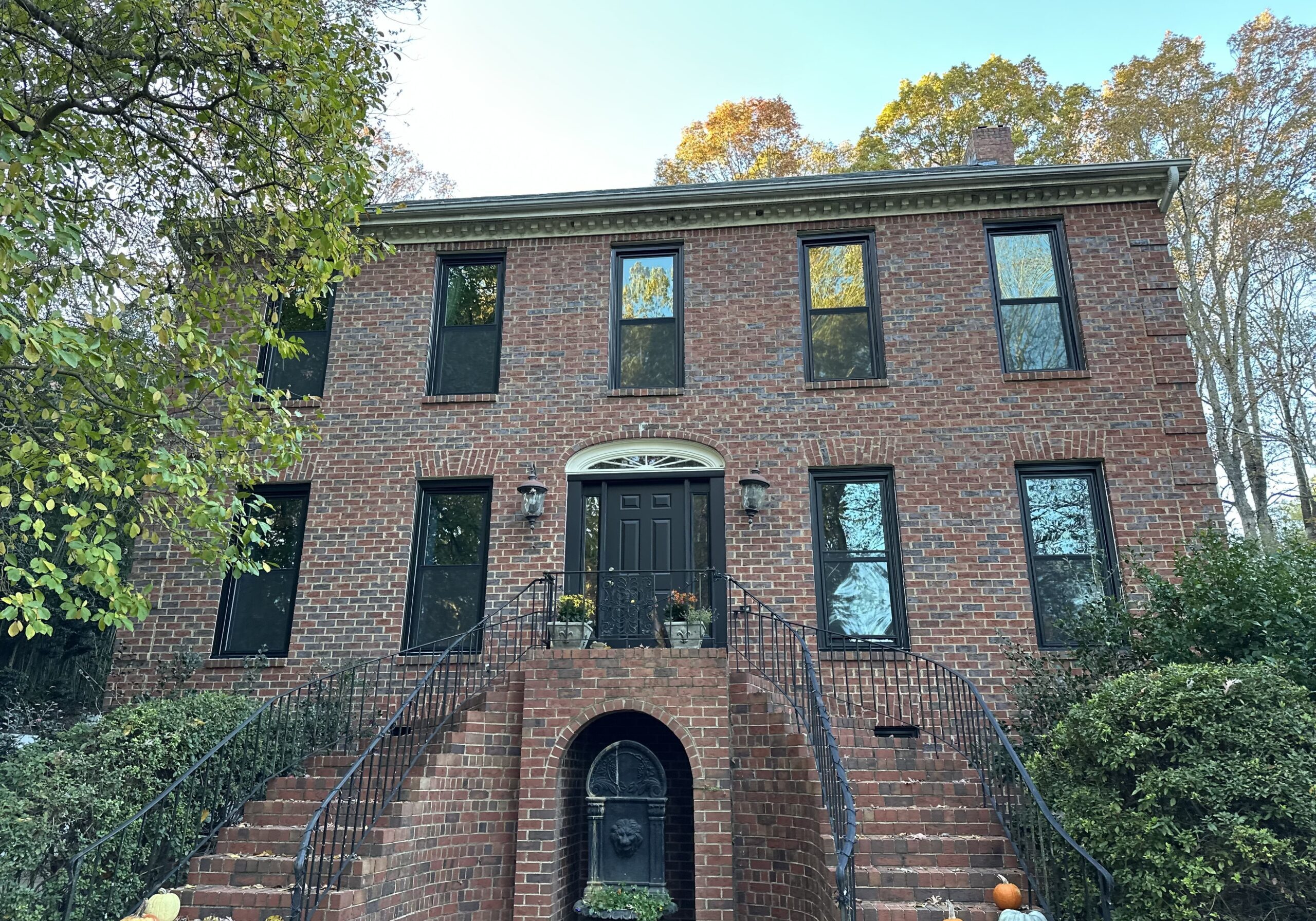 Red brick house with black-framed windows and double staircase, surrounded by greenery, near downtown Atlanta, Georgia.